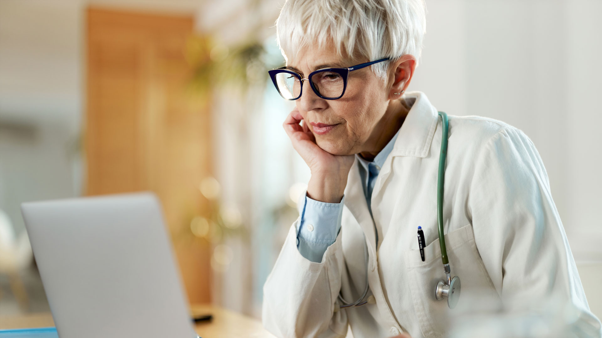 Pensive mature doctor working on a computer in her office at hospital.